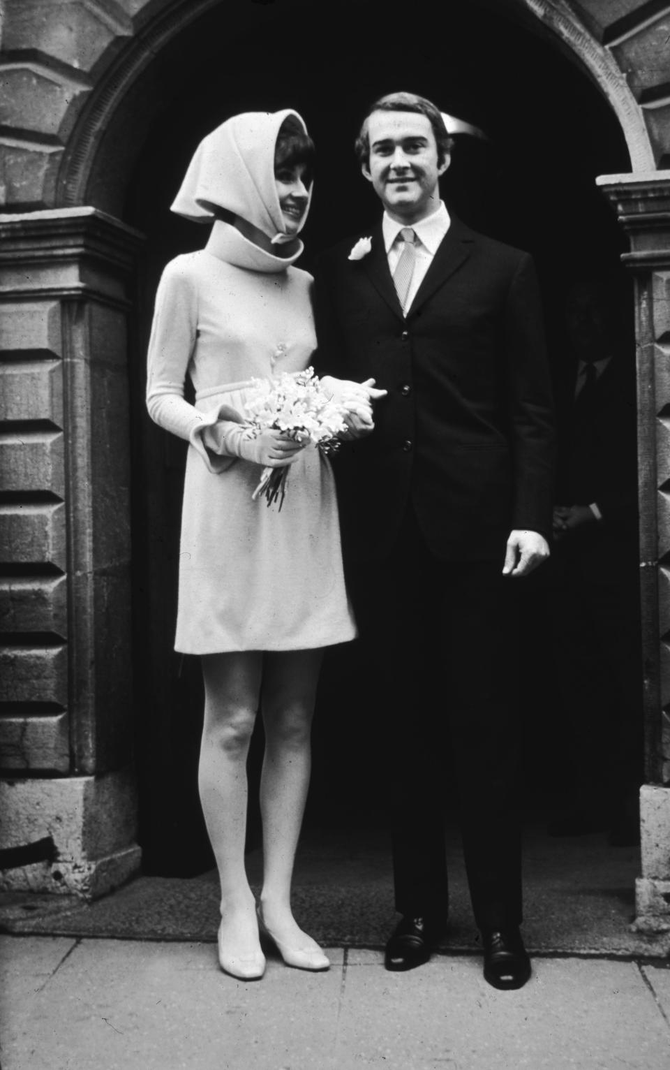 Audrey Hepburn in a headdress with a bouquet turns toward husband Andrea Dotti, who smiles.