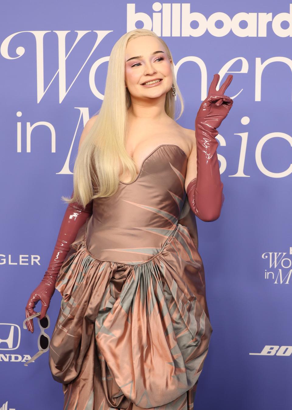Donning a two-tone bronze gown with mauve-colored latex gloves, Kim Petras lights up for the cameras at the 2023 Billboard Women in Music event.