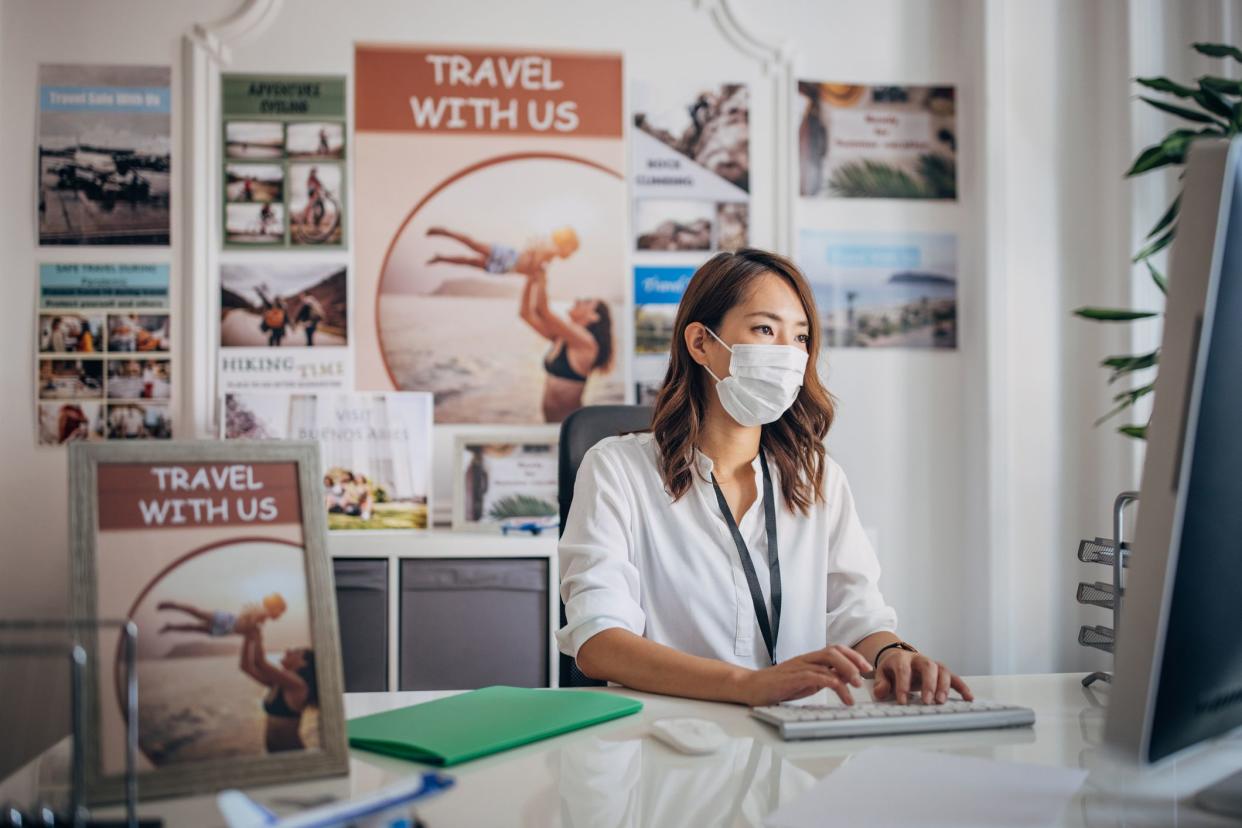 One woman, Japanese female working on computer in travel agency. She is wearing a protective face mask.