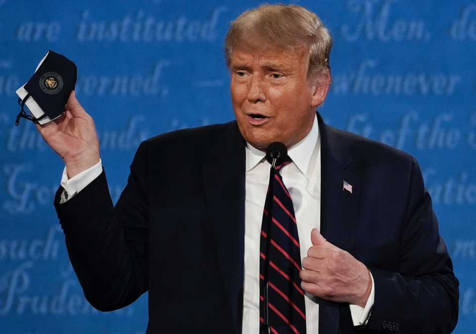 President Donald Trump holds up his facemask during the first presidential debate in Cleveland, Ohio on Sept. 29, 2020. (AP Photo/Julio Cortez, File)