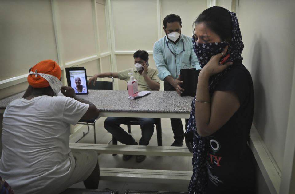 FILE - In this Friday, July 3, 2020, file photo, a man speaks with his mother who has been admitted in a COVID-19 hospital through a video phone facility by the COVID help desk, as another leaves crying after talking to her relative, outside a hospital, in New Delhi, India. In just three weeks, India's confirmed cases shot up from the world’s sixth to the third-worst hit country by the coronavirus pandemic, according to a tally by Johns Hopkins University. India's fragile health system was bolstered during stringent monthslong lockdown but could still be overwhelmed by an exponential rise in infections. (AP Photo/Manish Swarup, File)