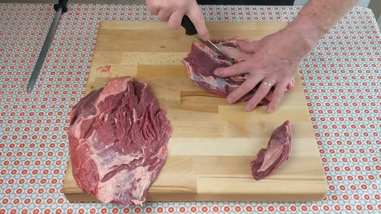 A pair of hands butchering beef knuckle on a cutting board