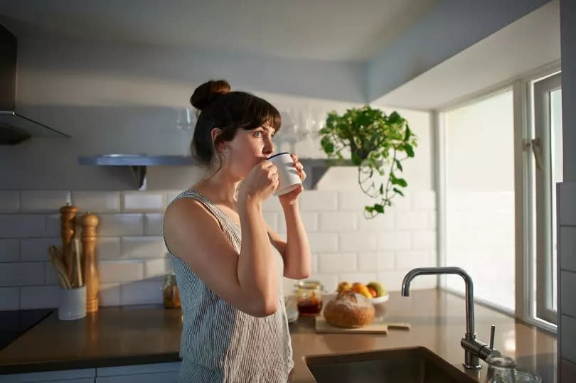 A woman standing in her kitchen drinks from a mug