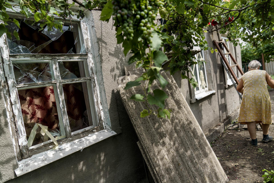 Nadiia Vasylivna, 70, walks by the blown out windows of her home from a rocket strike next door in Kramatorsk, Donetsk region, eastern Ukraine, Friday, Aug. 12, 2022. (AP Photo/David Goldman)