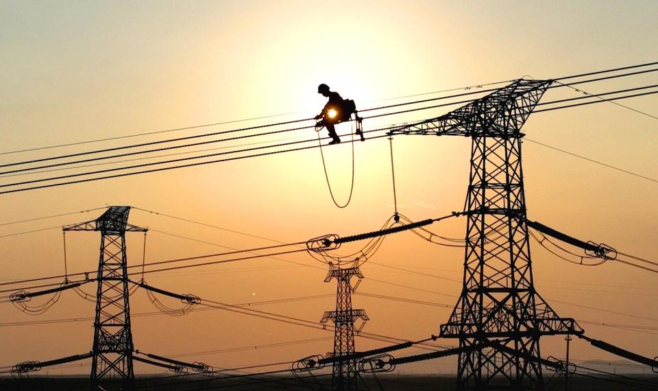 An electrical worker suspended on high-voltage powerlines in China against the sunset