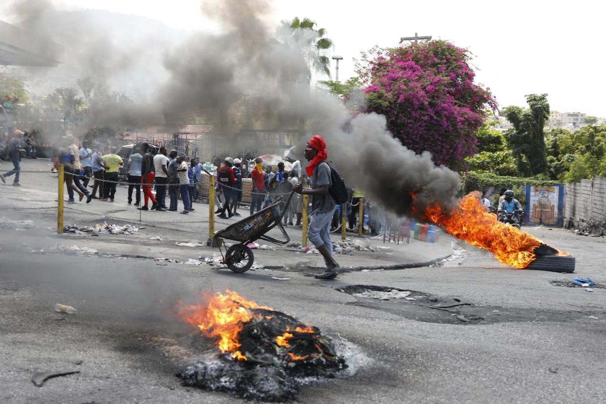 A man pushes a wheelbarrow past burning tires during a protest demanding the resignation of Prime Minister Ariel Henry in Port-au-Prince, Haiti on Thursday, March 7, 2024.  (AP/Odelyn Joseph - image credit)