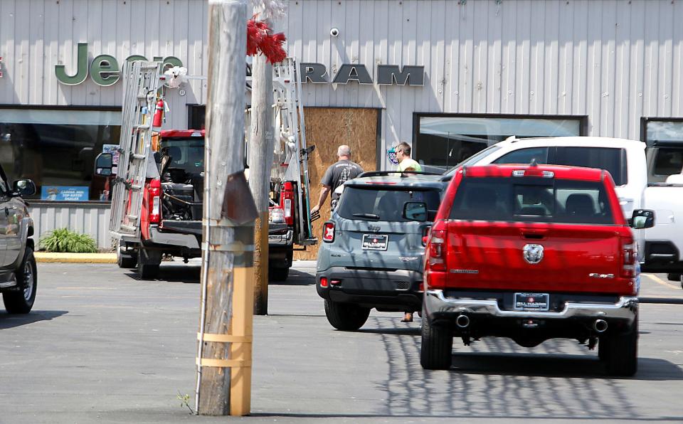 Workers replace the broken panes of glass at Bill Harris Chrysler Dodge Jeep and Ram on Baney Road after vehicles were stolen in the early morning hours on Thursday. TOM E. PUSKAR/TIMES-GAZETTE.COM