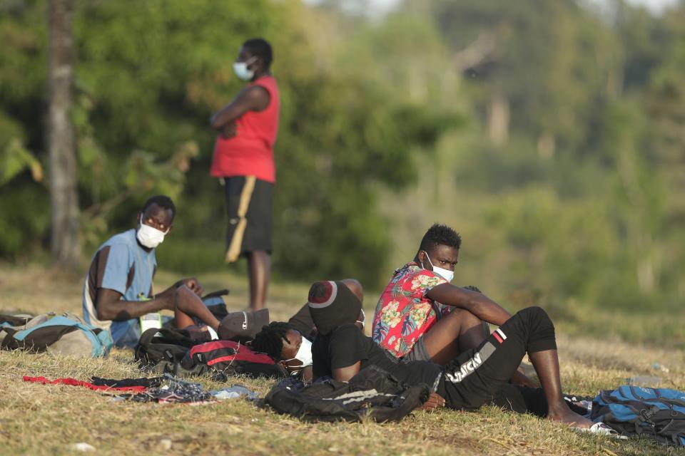 Haitian migrants sit on the grass at a migrant camp amid the new coronavirus pandemic in San Vicente, Darien province, Panama, Tuesday, Feb. 9, 2021. Panama is allowing hundreds of migrants stranded because of the pandemic, to move to the border with Costa Rica after just reopening its land borders. (AP Photo/Arnulfo Franco)