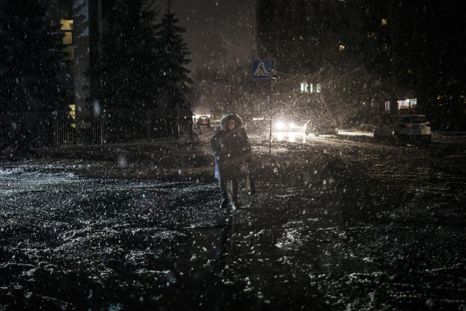 FILE - A woman crosses the street during snowfall, as power outages continue in Kyiv, Ukraine, Friday, Dec. 16, 2022. Russia's repeated attacks on Ukraine's energy infrastructure have left millions of civilians in the cold and the dark as temperatures plummet. (AP Photo/Felipe Dana, File)