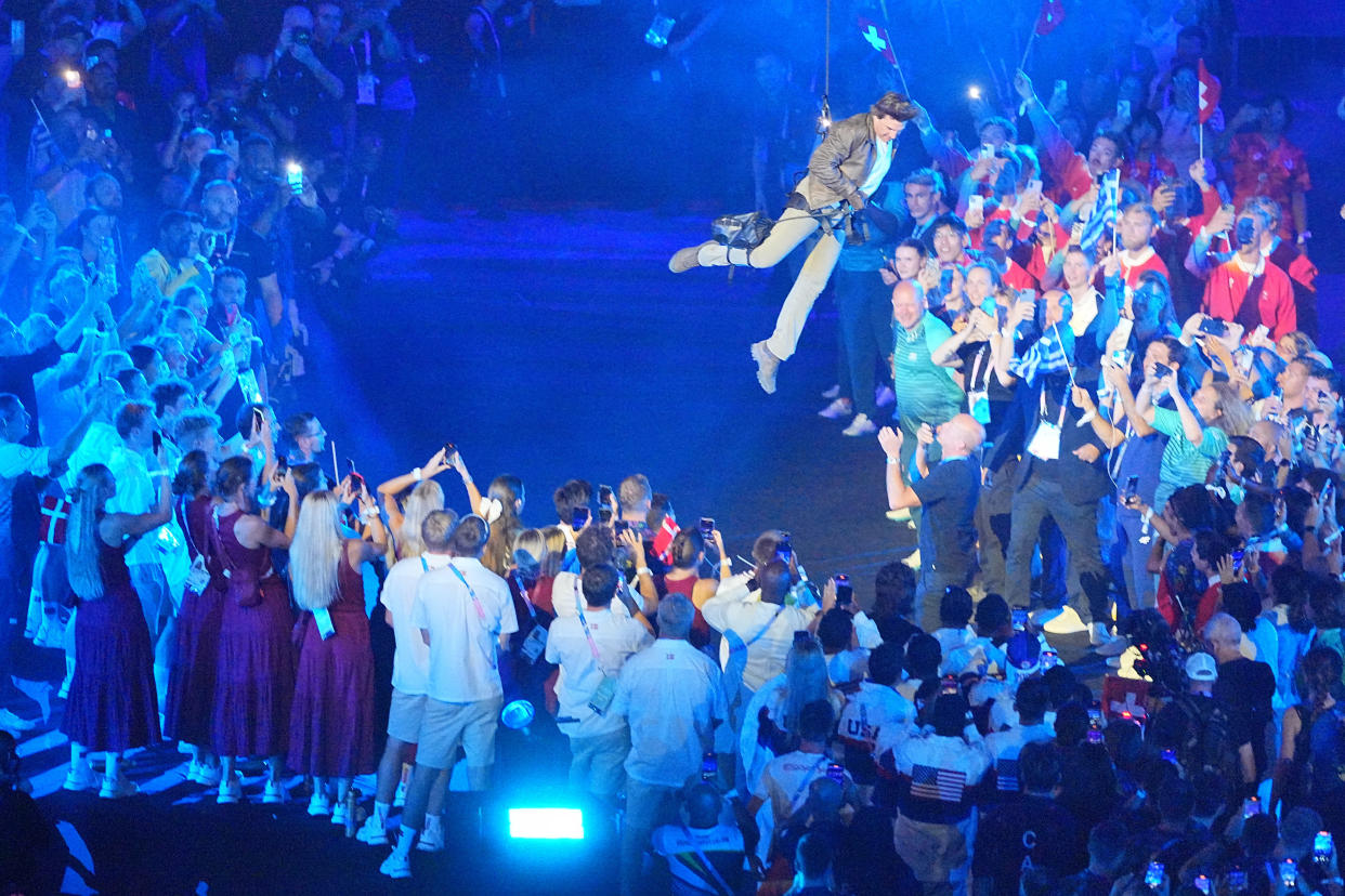 Tom Cruise is roped down into the stadium, where Olympic athletes await him, during the closing ceremony.