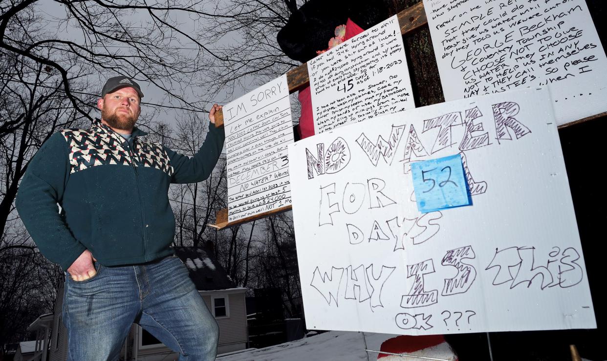 Tyler Miller, a Coventry Township resident who has been without well water since the communal well was capped in mid-December, stands next to the signs he has posted in front of his Pace Avenue home calling for trustees to help provide a solution.