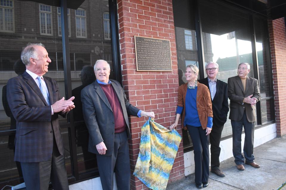 The partners of 301 Jackson Place, Patrick Moore (far left), Lindsey Torbett, Moore's wife Randall Moore, Thomas McBride and R.J. Dunn unveil a historical plaque for the building that McBride said was the oldest known commerical structure in Alexandria. The plaque is located on the side of the building facing Jackson Street.