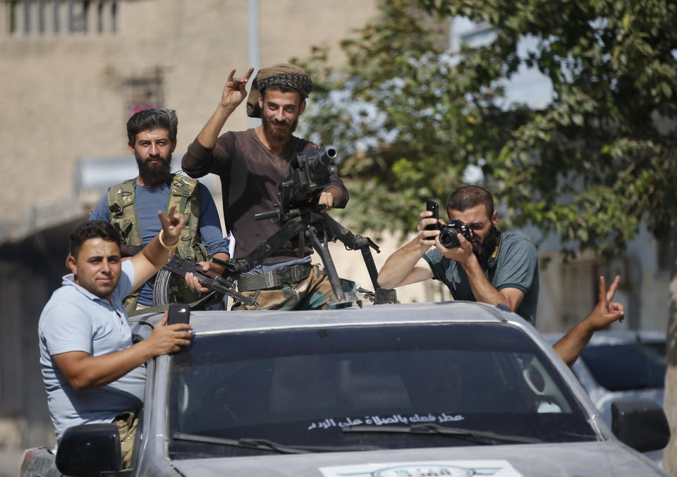 Turkish-backed Syrian opposition fighters cheer from a car as they drive around the border town of Akcakale, Sanliurfa province, southeastern Turkey, on their way to Tal Abyad, Syria, Monday, Oct. 14, 2019. Syrian troops entered Monday several northern towns and villages getting close to the Turkish border as Turkey's army and opposition forces backed by Ankara marched south in the same direction raising concerns of a clash between the two sides as Turkey's invasion of northern Syria entered its sixth day. (AP Photo/Lefteris Pitarakis)