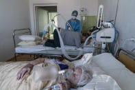 An elderly woman suffering from COVID-19 breathes with the help of an oxygen mask, foreground, as a nurse treats a patient in central district hospital of Kolomyia, western Ukraine, Tuesday, Feb. 23, 2021. After several delays, Ukraine finally received 500,000 doses of the AstraZeneca vaccine marketed under the name CoviShield, the first shipment of Covid-19 vaccine doses. The country of 40 million is one of the last in the region to begin inoculating its population. (AP Photo/Evgeniy Maloletka)