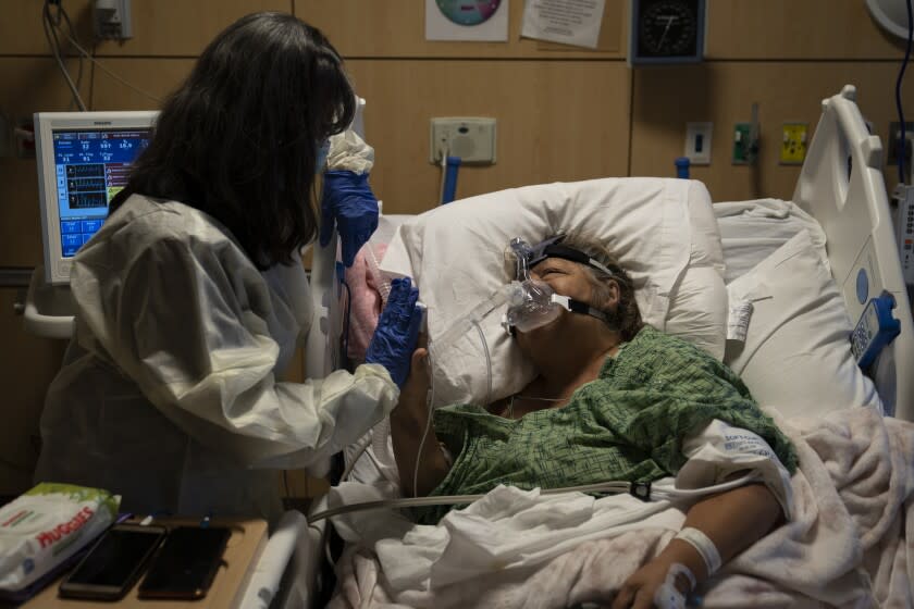 Becky Gonzalez, left, and her long time friend, Mary Lou Samora, a 71-year-old COVID-19 patient, put their palms together after they shared some encouraging words at Providence Holy Cross Medical Center in Los Angeles, Friday, Dec. 17, 2021. (AP Photo/Jae C. Hong)