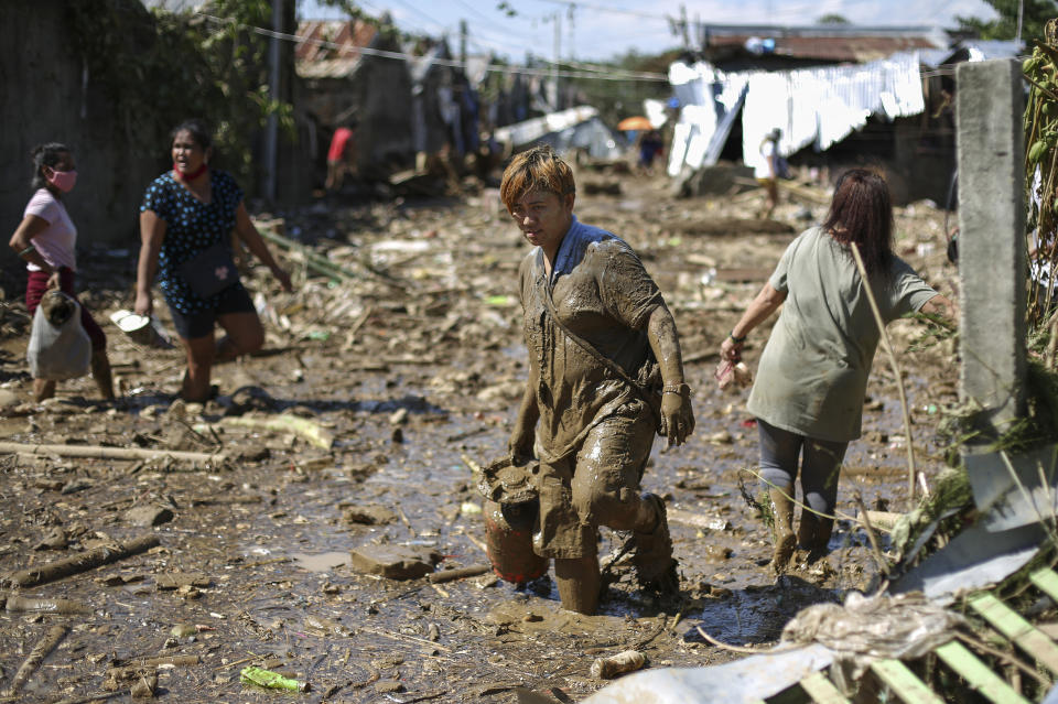 Gina Belchez carries a gas-stove through mud and debris in the typhoon-damaged Kasiglahan village in Rodriguez, Rizal province, Philippines on Friday, Nov. 13, 2020. Thick mud and debris coated many villages around the Philippine capital Friday after Typhoon Vamco caused extensive flooding that sent residents fleeing to their roofs and killing dozens of people. (AP Photo/Aaron Favila)