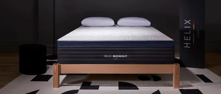  Helix Midnight Luxe mattress review image shows the hybrid bed on a wooden bed frame on a black and white rug. 