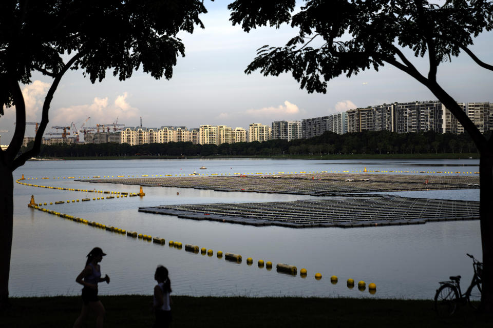 Joggers pass by a floating solar panel farm on the Bedok Reservoir lined by apartment buildings in Singapore, Sunday, July 16, 2023. In 2006 the government launched the Active, Beautiful, Clean Waters Program which transformed the country's water systems into more public areas for the public to enjoy. Through the program, reservoirs are now areas where residents can kayak, hike and picnic, giving a greater sense of ownership and value to the country's water supplies. (AP Photo/David Goldman)