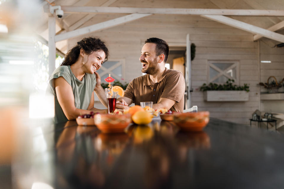 Two people smiling and sitting at a table with fruit, appearing to enjoy a conversation