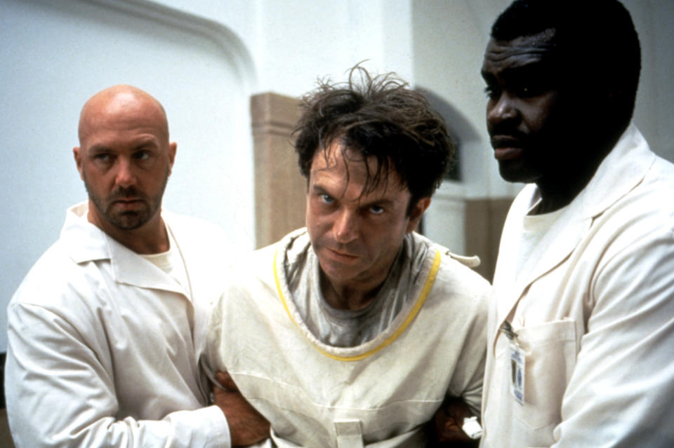 Kevin Rushton and Gene Mack holding Sam Neill in a straight jacket