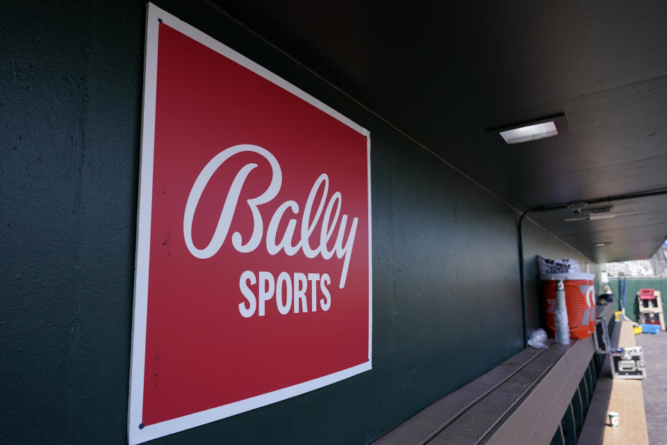 FILE - A Bally Sports logo is shown in the dugout during a spring training baseball game at Roger Dean Stadium, Saturday, March 4, 2023, in Jupiter, Fla. Amazon will partner with the Diamond Sports as part of a restructuring agreement as the largest owner of regional sports networks looks to emerge from bankruptcy. Diamond owns 18 networks under the Bally Sports banner. Those networks have the rights to 37 professional teams — 11 baseball, 15 NBA and 11 NHL.(AP Photo/Lynne Sladky, File)