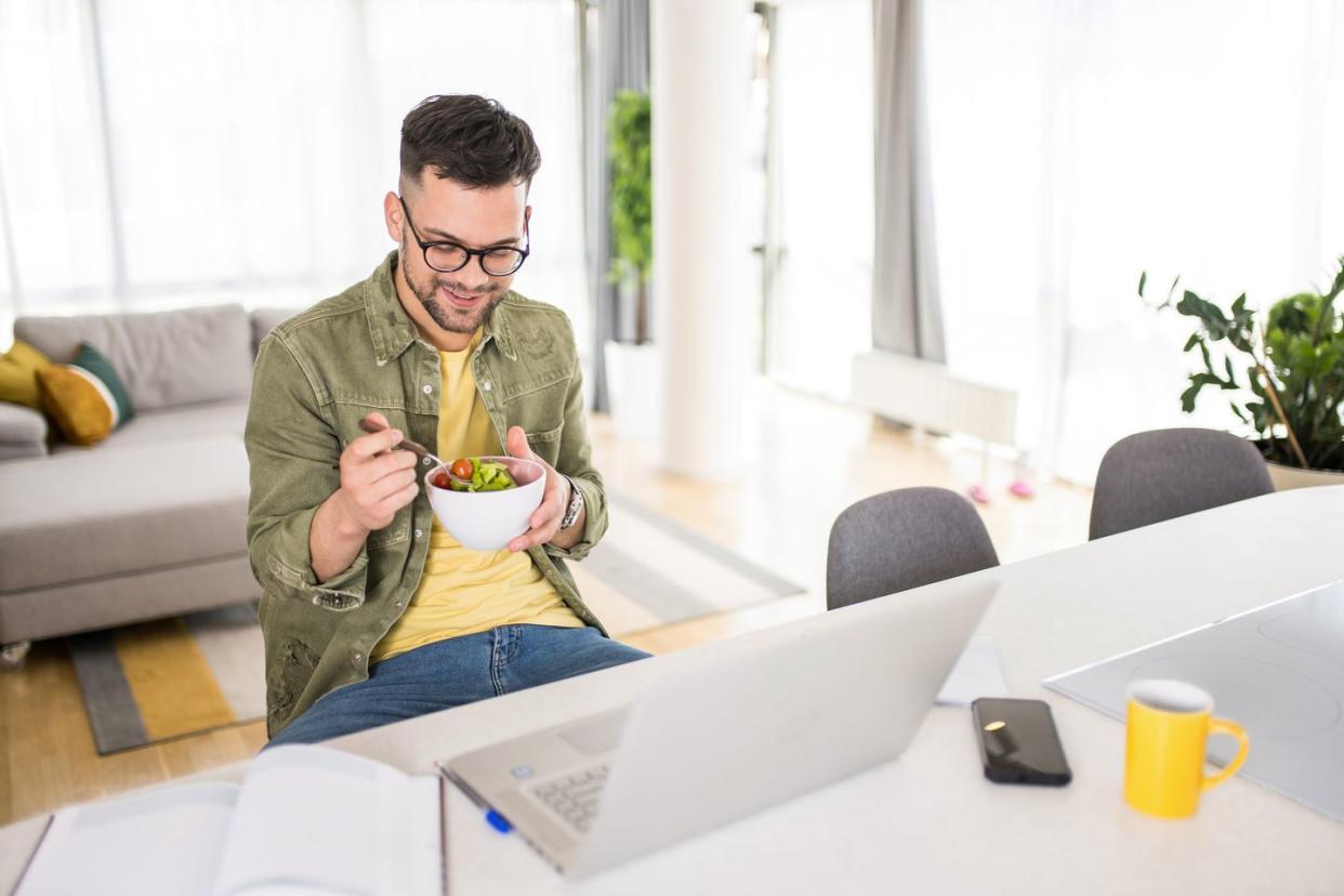 young man eating a salad while working in comfort of his home