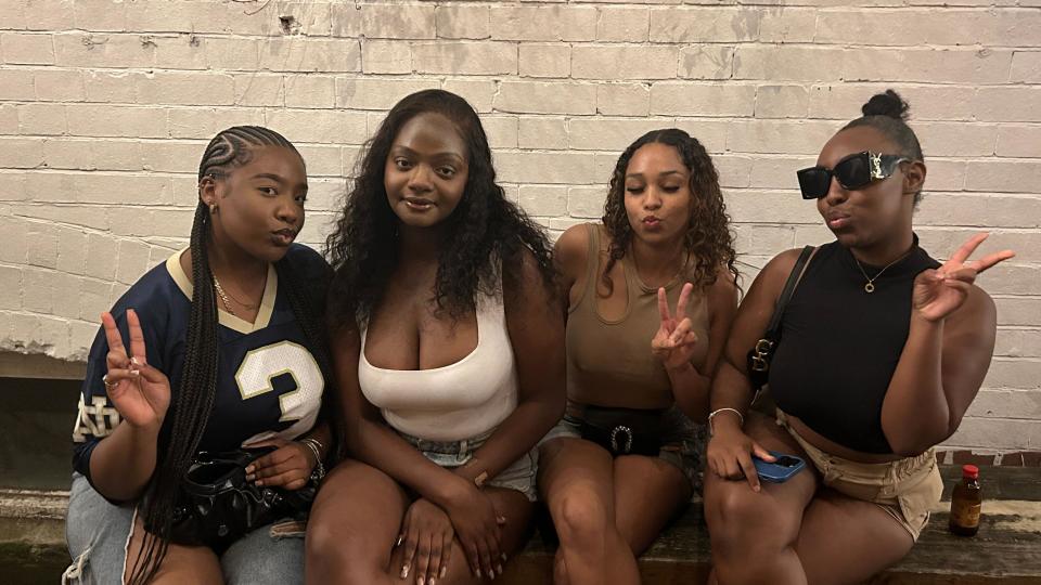 Group of four friends, Layla, Leah, Hermione, Kamorae - sitting down on a wooden bench, with three of them holding up "peace" signs.