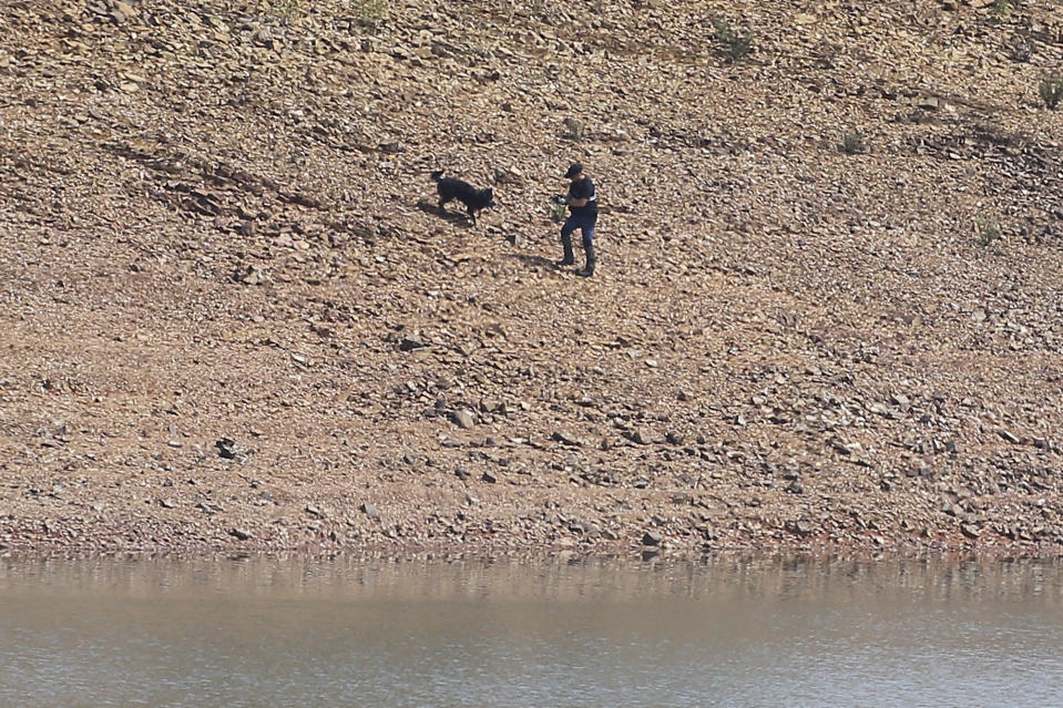 A police officer and a dog work at the Arade dam near Silves, Portugal, Tuesday May 23, 2023. Portuguese police aided by German and British officers have resumed their search for Madeleine McCann, the British child who disappeared in the country's southern Algarve region 16 years ago. Some 30 officers could be seen in the area by the Arade dam, about 50 kilometers (30 miles) from Praia da Luz, where the 3-year-old was last seen alive in 2007. (AP Photo/Joao Matos)