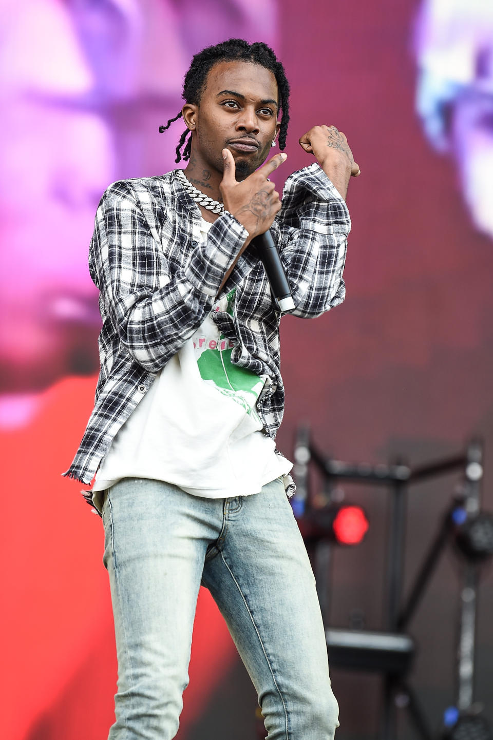 Playboi Carti performing at Wireless Festival, wearing a Black and white flannel shirt, white, green and red t-shirt, and blue jeans.