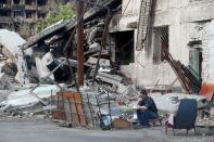 A man sits in a courtyard outside a damaged building in Mariupol