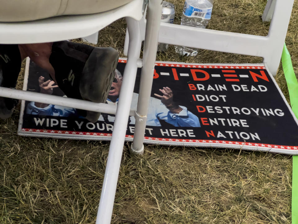 FILE - A man sits with his feet on a doormat critical of President Joe Biden during the ReAwaken America Tour at Cornerstone Church in Batavia, N.Y., Aug. 13, 2022. (AP Photo/Carolyn Kaster, File)