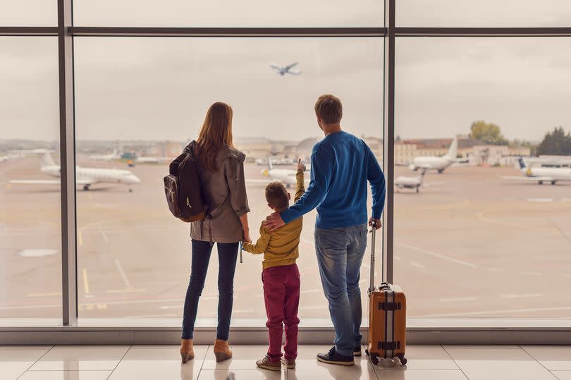 Back view shot of young family with luggage standing near window in airport before boarding