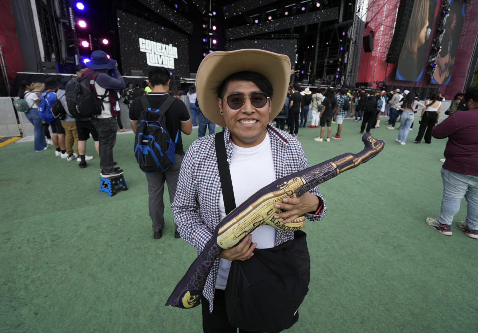 FILE - A fan poses for a photo with an inflatable AK-47 inflatable at the Arre Music Festival which features Mexican regional music, in Mexico City, Sept. 9, 2023. (AP Photo/Fernando Llano, File)