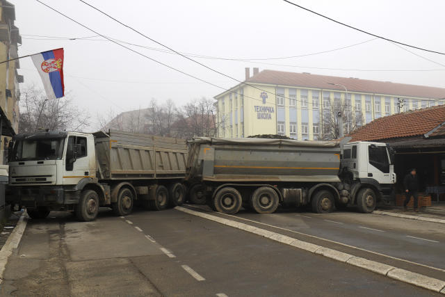 A man passes by a barricade made of trucks loaded with stones that was erected during the night on a street in northern, Serb-dominated part of ethnically divided town of Mitrovica, Kosovo, Tuesday, Dec. 27, 2022. Serbia on Monday placed its security troops on the border with Kosovo on "the full state of combat readiness," ignoring NATO's calls for calming down of tensions between the two wartime Balkan foes. (AP Photo/Bojan Slavkovic)