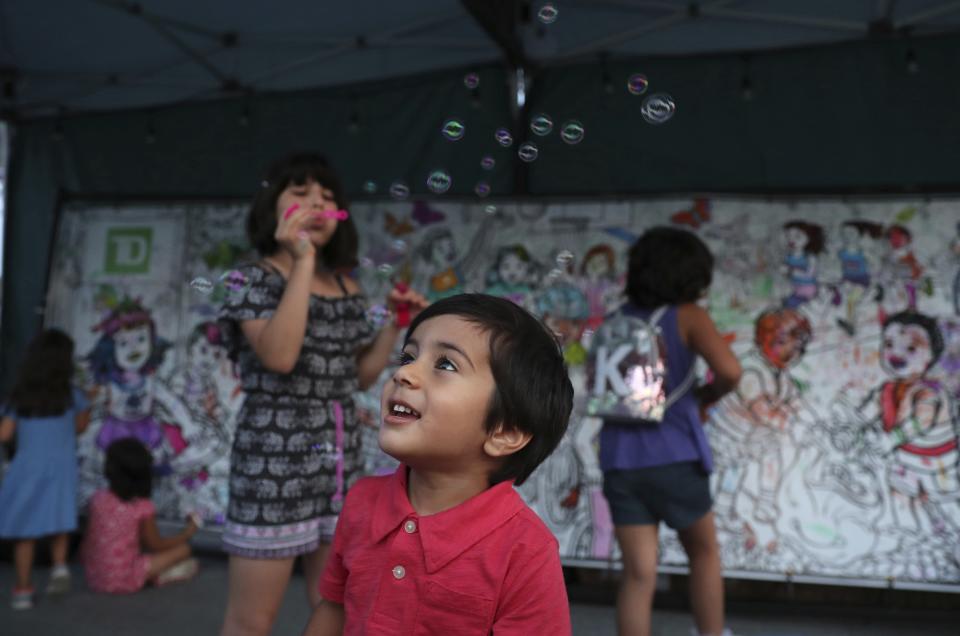 In this Friday, July 26, 2019 photo, a boy enjoys the bubbles blowing by a girl in front of a painting board showing the Canadian lifestyle for the children in Tirgan summer festival at the Harbourfront Centre in Toronto, Canada. The event aims to preserve and celebrate Iranian and Persian culture, said festival CEO Mehrdad Ariannejad. Among those who attended were second-and third-generation immigrants, many of whom have never been to Iran or have not been there since leaving the country following the 1979 Islamic Revolution. (AP Photo/Kamran Jebreili)