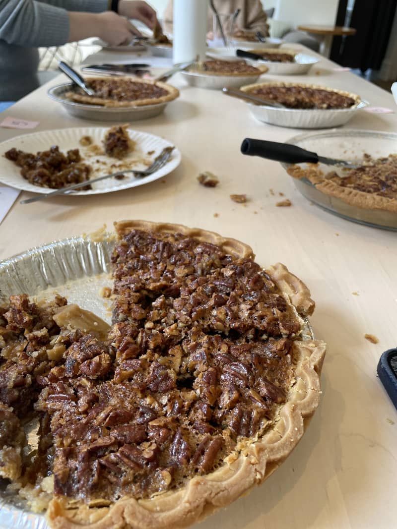 pecan pies on table in silver tins with pieces taken out and crubs on table