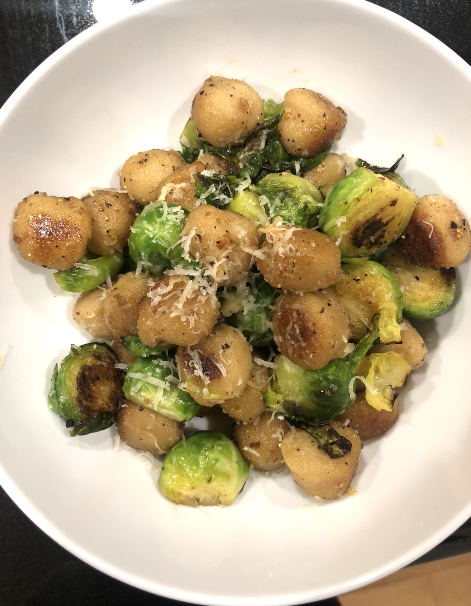 A bowl containing sautéed scallops and Brussels sprouts, topped with grated cheese