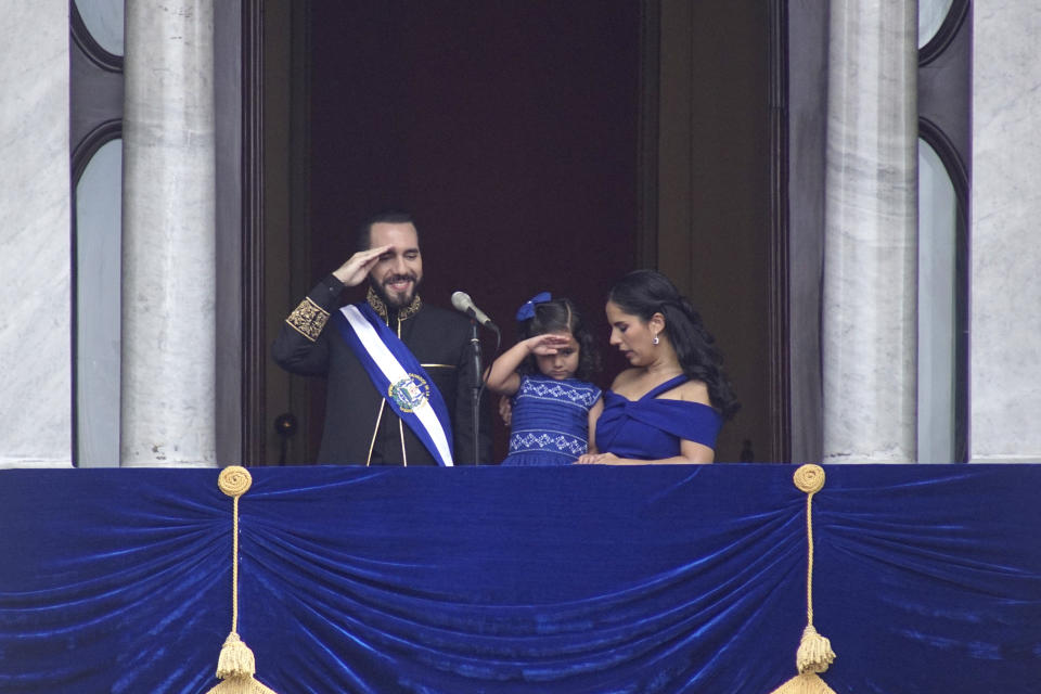 El presidente de El Salvador, Nayib Bukele, y su hija Layla saludan mientras están de pie en un balcón con la primera dama Gabriela Roberta Rodríguez, luego de que éste prestó juramento para un segundo mandato, en San Salvador, El Salvador, el sábado 1 de junio de 2024. (Foto AP/ Salvador Meléndez)