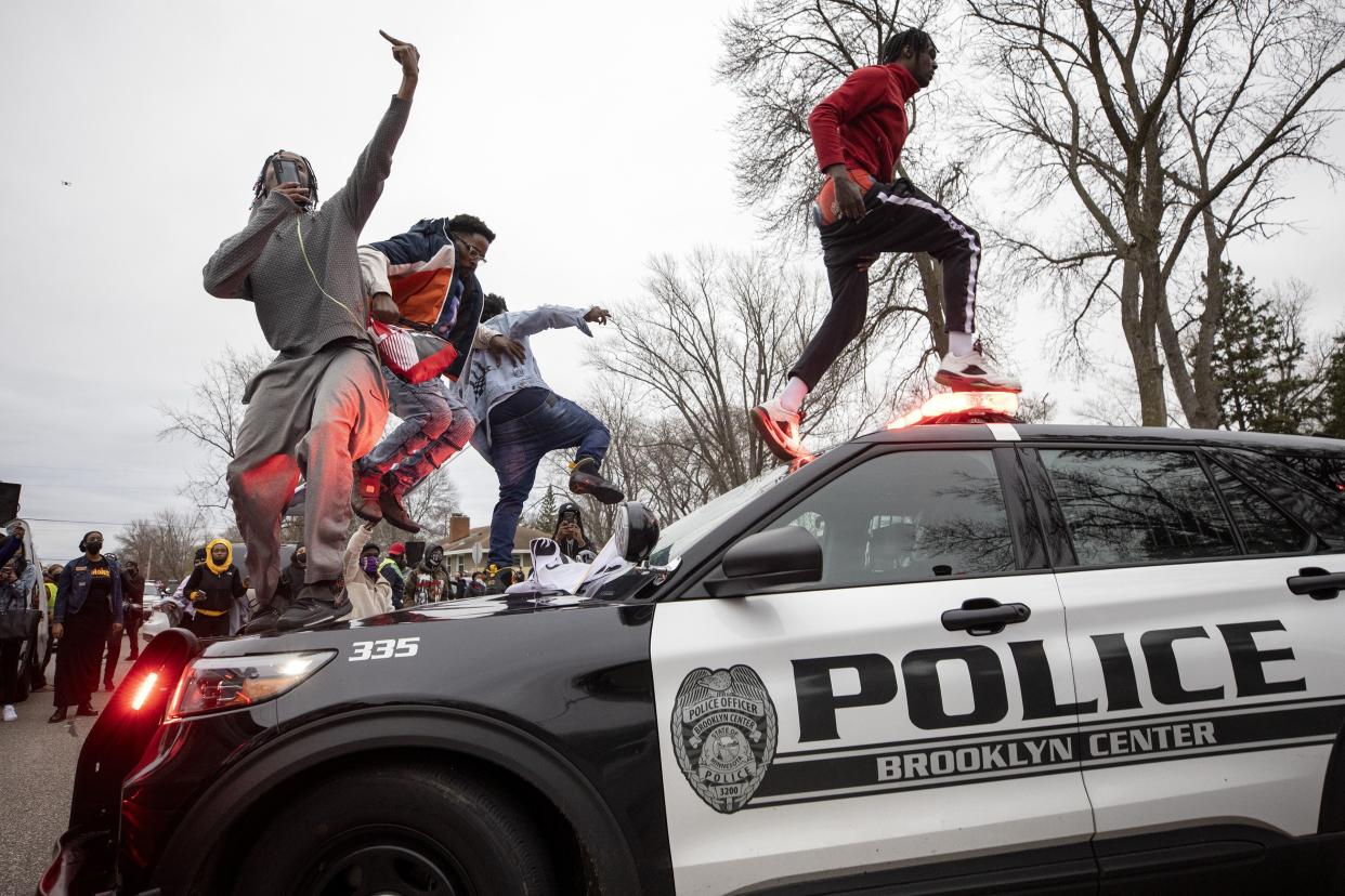 Men jump on police vehicles near the site of a shooting involving a police officer, Sunday, April 11, 2021, in Brooklyn Center, Minn.