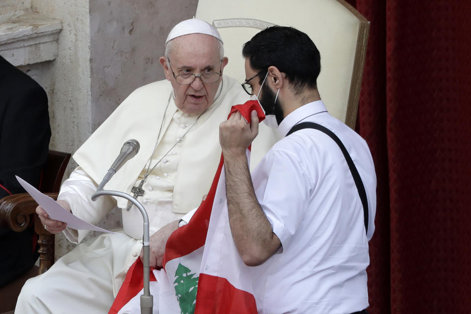 Pope Francis speaks to Lebanese priest Georges Breidi, right, as they hold a Lebanese flag in remembrance of last month's explosion in Beirut, during the pontiff's general audience, the first with faithful since February when the coronavirus outbreak broke out, at the San Damaso courtyard, at the Vatican, Wednesday, Sept. 2, 2020. (AP Photo/Andrew Medichini)