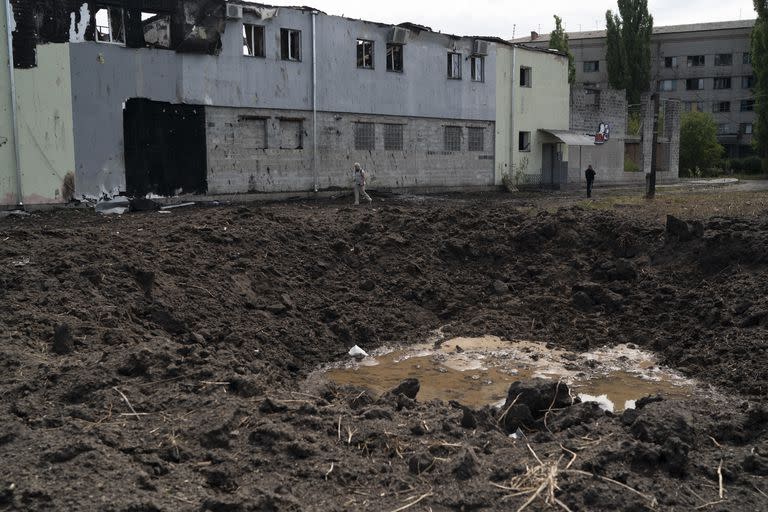 Dos personas caminan junto a un cráter creado por un ataque ruso en un área cercana a la Sociedad de la Cruz Roja ucraniana, el lunes 5 de septiembre de 2022, en Sloviansk, Ucrania. (AP Foto/Leo Correa)