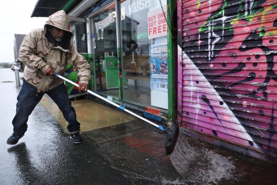 A worker uses a broom to sweep rain water from a shop along the Venice Beach Boardwalk (REUTERS)