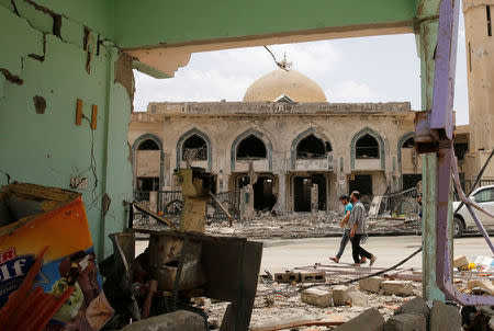 Iraqi men walk past a damaged building after the end of the battles between the Iraqi forces and Islamic State militants at their district in western Mosul, Iraq, April 30, 2017. REUTERS/Muhammad Hamed