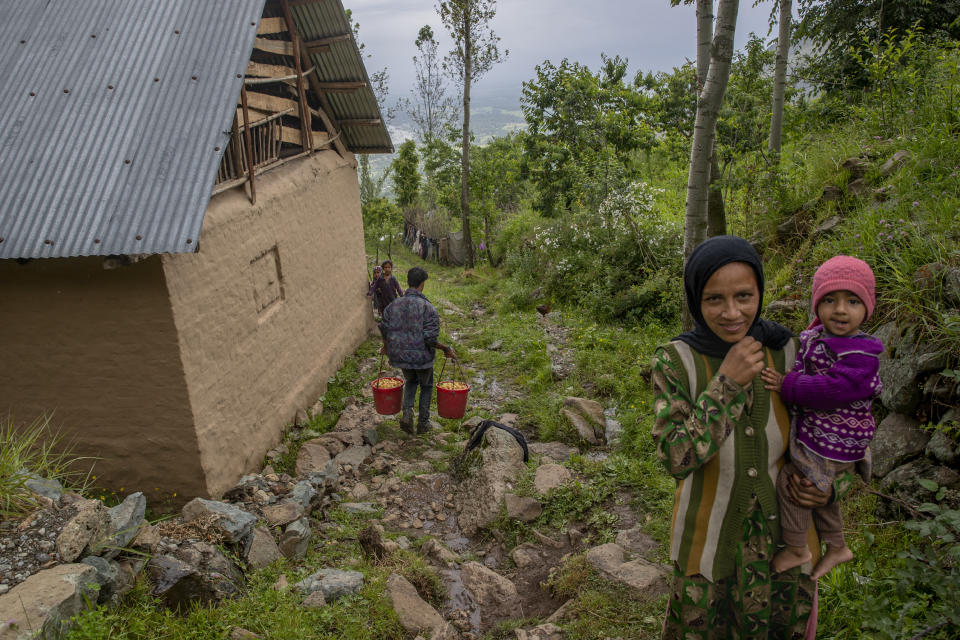 A Kashmiri farmer walks carrying cherries freshly plucked from a nearby orchard as a Kashmiri woman and her child react to the camera in Waliwar village, north east of Srinagar, Indian controlled Kashmir, Wednesday, June 16, 2021. Cherry farmers in Kashmir who were not able get most of their produce to the markets last year because of the COVID-19 pandemic are hoping for good returns this year. (AP Photo/ Dar Yasin)