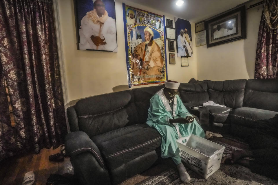 Imam Omar Niass checks his phone while sorting a delivery of city identification cards approved for African migrants at Bronx's Masjid Ansaru-Deen mosque, Friday March 15, 2024, in New York. Imam Niass has repurposed the mosque, formerly his family home, as a shelter for African migrants seeking asylum in the United States, providing a physical address where they can receive mail. (AP Photo/Bebeto Matthews)