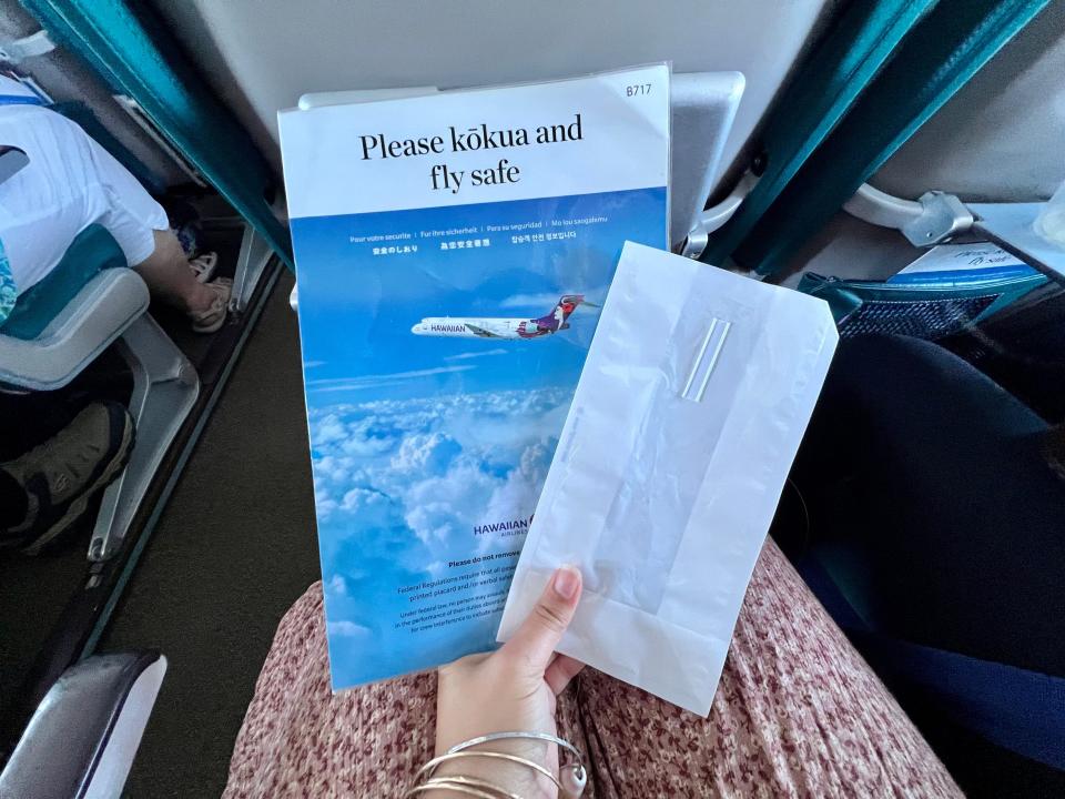 The writer holds a pamphlet on a plane saying "Please kokua and fly safe"