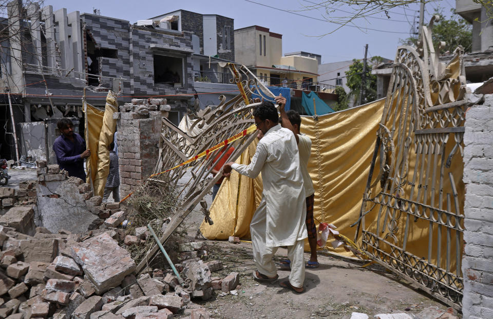 Residents remove a gate from their damaged house at the site of a car bombing Wednesday, in Lahore, Pakistan, Thursday, June 24, 2021. Pakistani security forces on Thursday arrested one of the alleged perpetrators of the car bombing that killed at least three people and wounded some 25 others near the residence of a jailed anti-India militant leader Hafiz Saeed, in the eastern city of Lahore, officials said. (AP Photo/K.M. Chaudary)