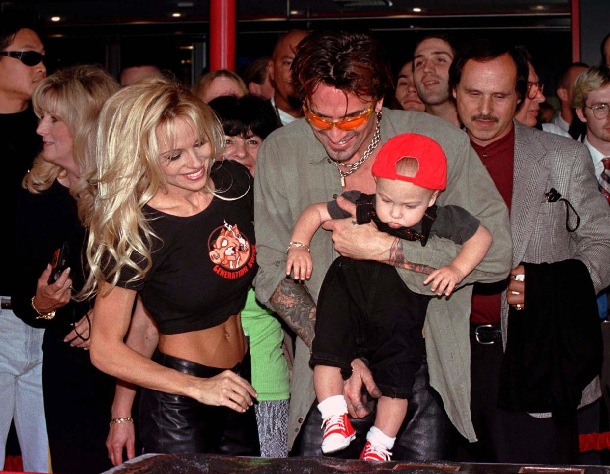 Actress Pamela Anderson Lee (L) looks on as husband, musician Tommy Lee holds their son, Brandon Thomas Lee, above the cement plaque where Tommy Lee's rock group 