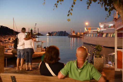 People watch as the sun rises over the stranded Costa Concordia cruise ship near the harbour of Giglio Porto. Salvage crews in July began preliminary work on preparations to refloat the half-submerged cruise liner in what is set to be the biggest ever operation of its kind