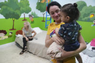 Isabel Bembow Tamayo holds Liam Centeno, 1, in the Iglesia Rescate school classroom that is converted into a bedroom for her family, Tuesday, Feb. 21, 2023, in Hialeah, Fla. Isabel, her mother and two siblings arrived on an overcrowded boat from Cuba. In the last 18 months, an estimated 250,000 migrants and asylum-seekers like her, mostly from Cuba, Nicaragua, Venezuela and Haiti, have made their way to the Miami area, with only precarious legal status and often without work permits. (AP Photo/Marta Lavandier)